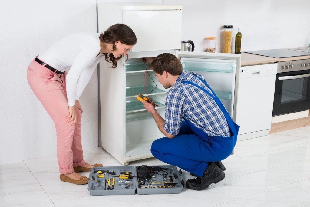 housewife looking at worker repairing the fridge