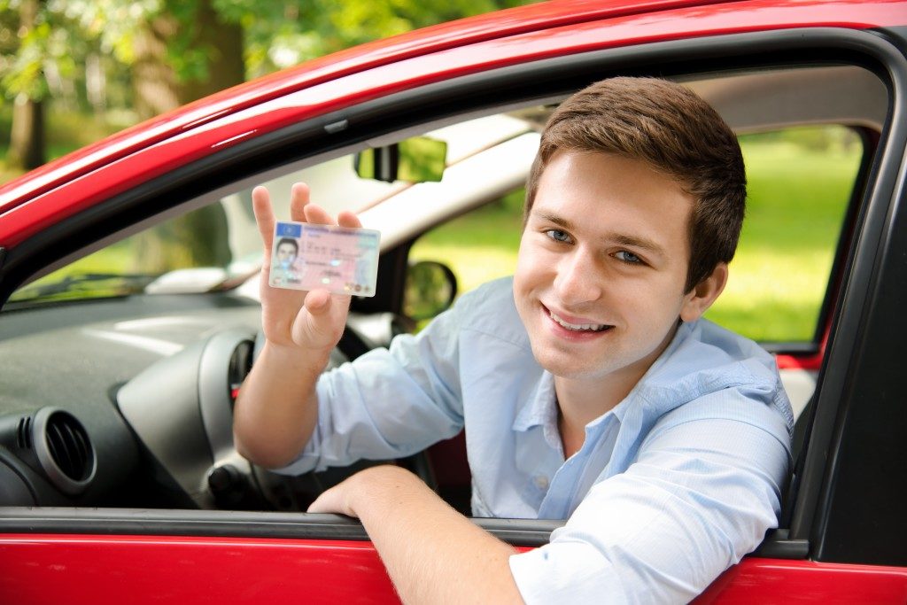 teenager sitting in new car and showing his driver's license