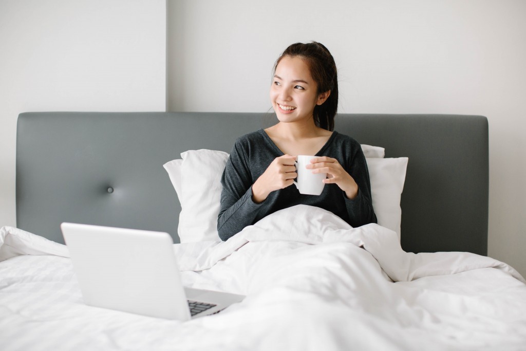 millenial in bed with coffee and laptop