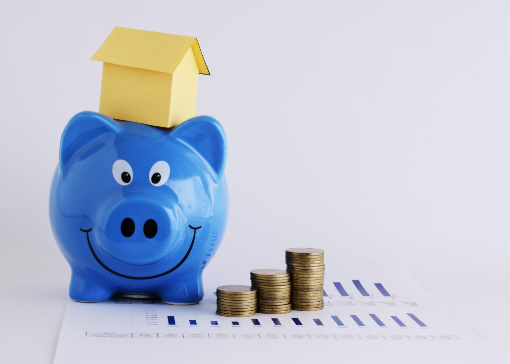 blue piggy bank with house on its head and coins beside it