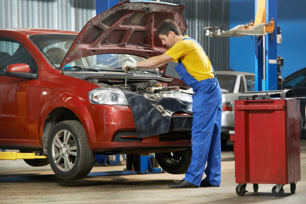 mechanic wearing blue coveralls working on a hood of a red suv